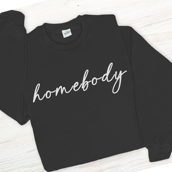 Black sweatshirt with 'homebody' text on a white wooden surface