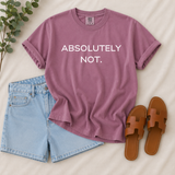 A mauve short-sleeve T-shirt with the text 'ABSOLUTELY NOT.' in white, styled in a flat lay with light blue denim shorts, brown slide sandals, and a green plant on a cream fabric background.