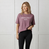 Woman wearing a mauve t-shirt with 'ABSOLUTELY NOT.' text against a white paneled wall.