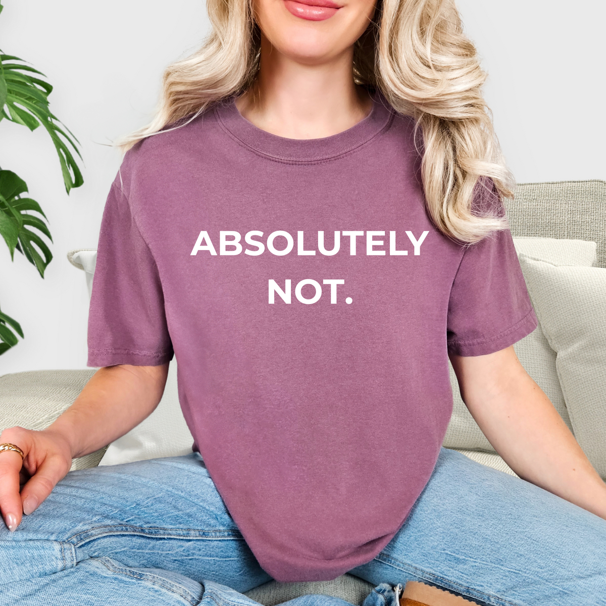 Person wearing a purple t-shirt with 'ABSOLUTELY NOT.' text, sitting on a couch.
