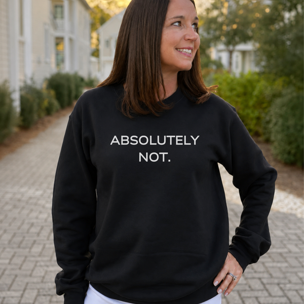 A woman wearing a black crewneck sweatshirt with the text 'ABSOLUTELY NOT.' printed in white capital letters on the chest, standing outdoors on a paved walkway.