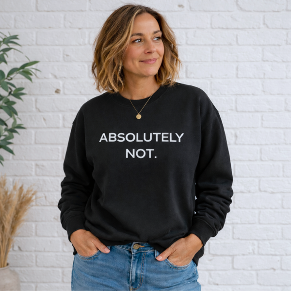 A woman standing in a black sweatshirt with the words "Absolutely Not" in white text and jeans, casually leaning in front of a brick wall.