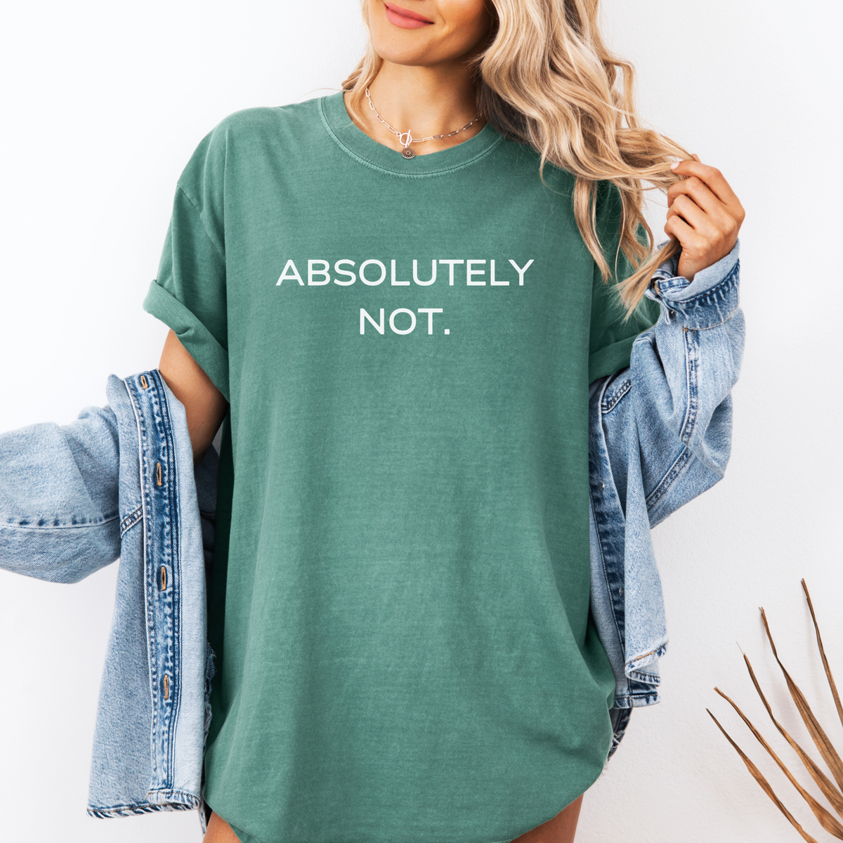 Woman wearing a green t-shirt with 'ABSOLUTELY NOT.' text, holding a denim jacket.