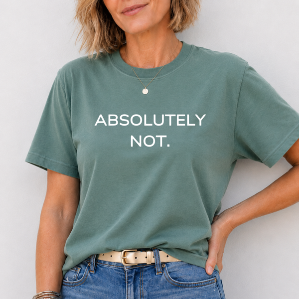 A woman wearing a sage green graphic t-shirt with the text 'ABSOLUTELY NOT.' printed in white capital letters across the chest, paired with blue jeans and a beige belt.