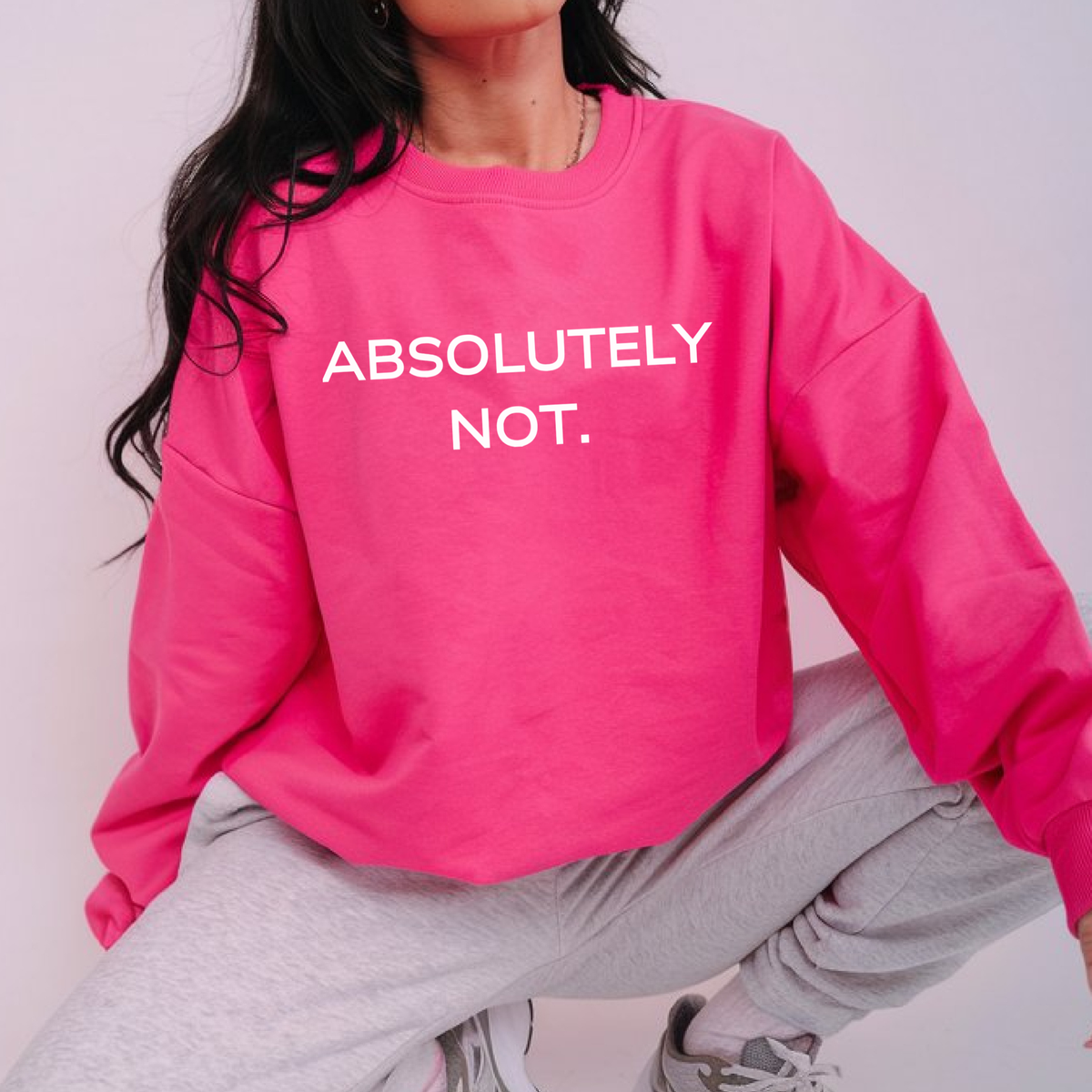 A woman wearing a bright pink sweatshirt with 'ABSOLUTELY NOT.' text & wearing sweatpants.