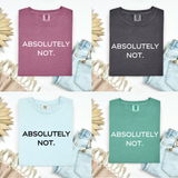 Four folded graphic T-shirts arranged in a 2x2 grid with denim jeans and decorative dried flowers around them. The shirts are in dusty pink, charcoal gray, light blue, and mint green, each printed with the text 'ABSOLUTELY NOT.