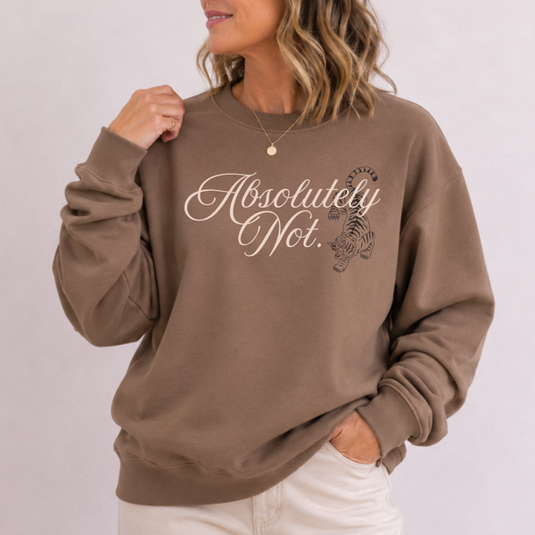 A woman wearing a brown crewneck sweatshirt with 'Absolutely Not.' and a tiger graphic printed on the front, paired with off-white pants against a light gray background.