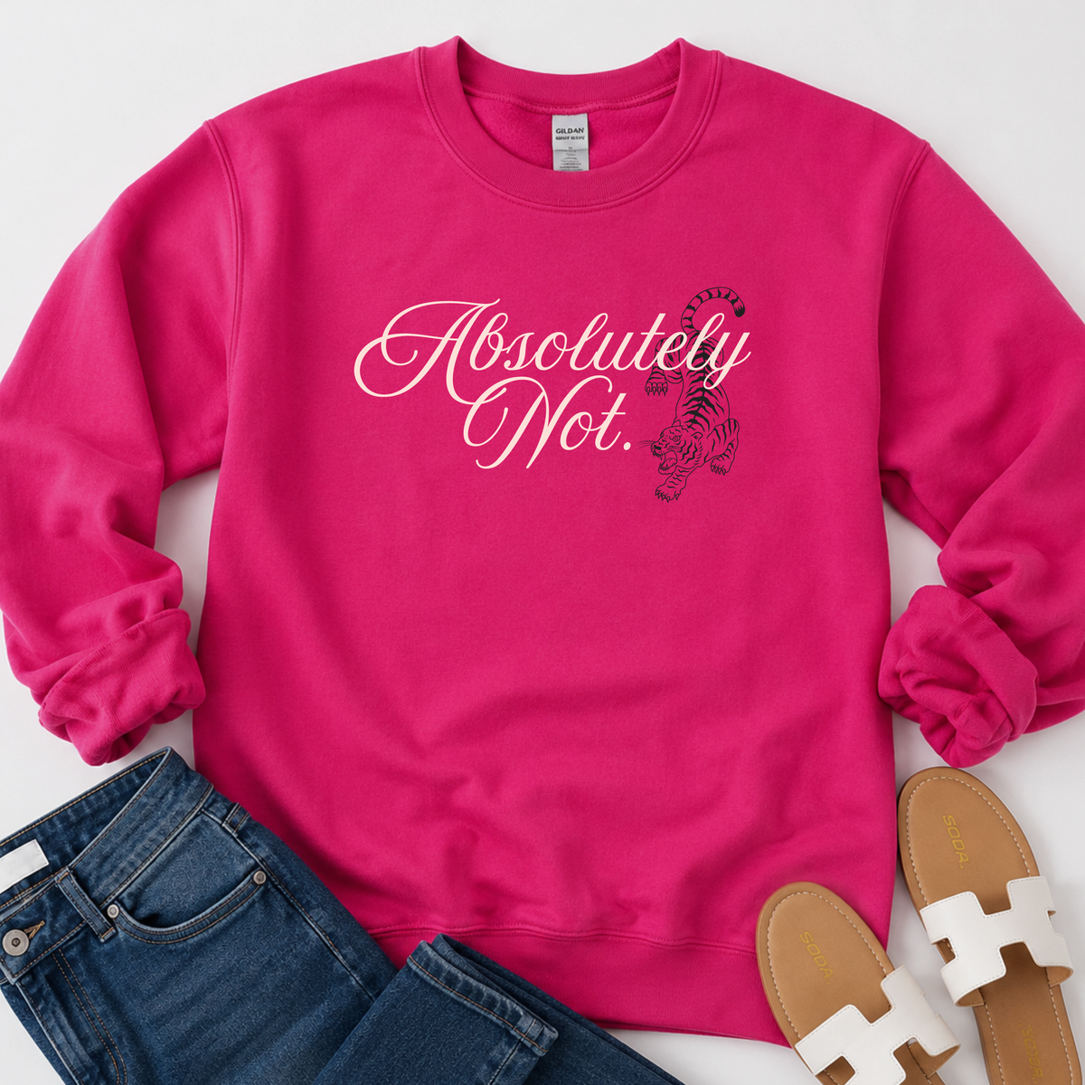 A bright pink crewneck sweatshirt laid flat on a white background, styled with blue jeans and tan sandals. The sweatshirt features the phrase 'Absolutely Not.