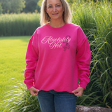 A woman wearing a bright pink crewneck sweatshirt with the text 'Absolutely Not.' in white script and a small black graphic, standing outdoors in front of green grass and plants.