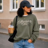 A woman wearing an olive green sweatshirt with the text 'Absolutely Not.' in white script and a small black graphic, paired with blue jeans, a black baseball cap, and carrying a black shoulder bag while holding an iced coffee outdoors.