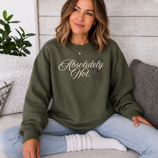 A woman sitting cross-legged on a couch wearing an olive green sweatshirt with the text 'Absolutely Not.' in white script and a small black snake graphic.