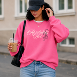 A woman wearing a bright pink crewneck sweatshirt with 'Absolutely Not' in white script and a small black-and-white tiger graphic, paired with a black baseball cap, blue jeans, and a black shoulder bag while holding an iced coffee.