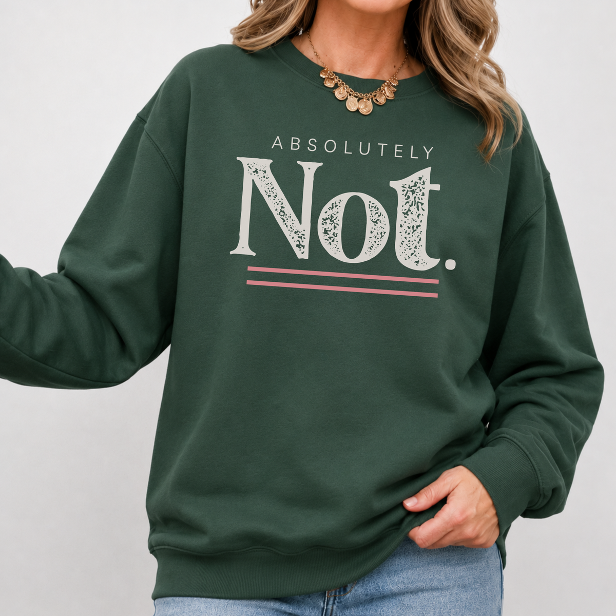 A woman wearing a dark green crewneck sweatshirt with a graphic print that reads 'ABSOLUTELY Not.' in white, with pink double horizontal lines underneath.