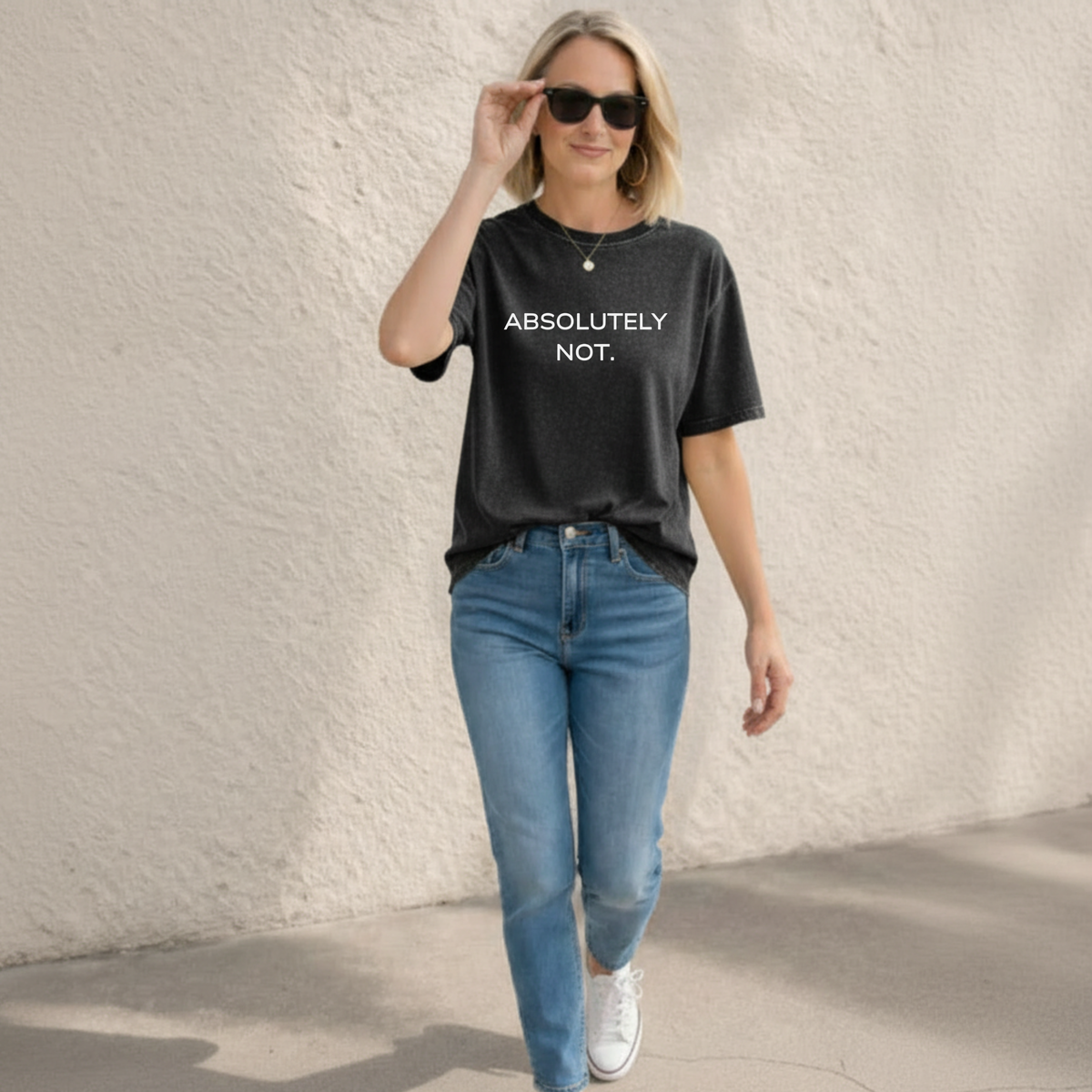 Woman wearing a black t-shirt with 'ABSOLUTELY NOT.' text and blue jeans against a light textured wall.
