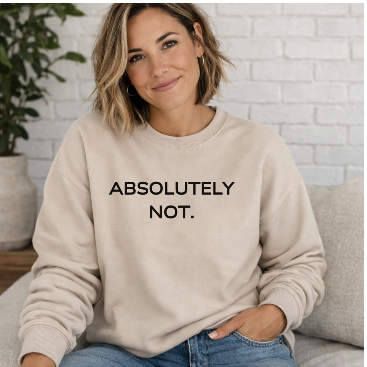 Woman wearing a beige sweatshirt with 'ABSOLUTELY NOT.' text, sitting on a couch.