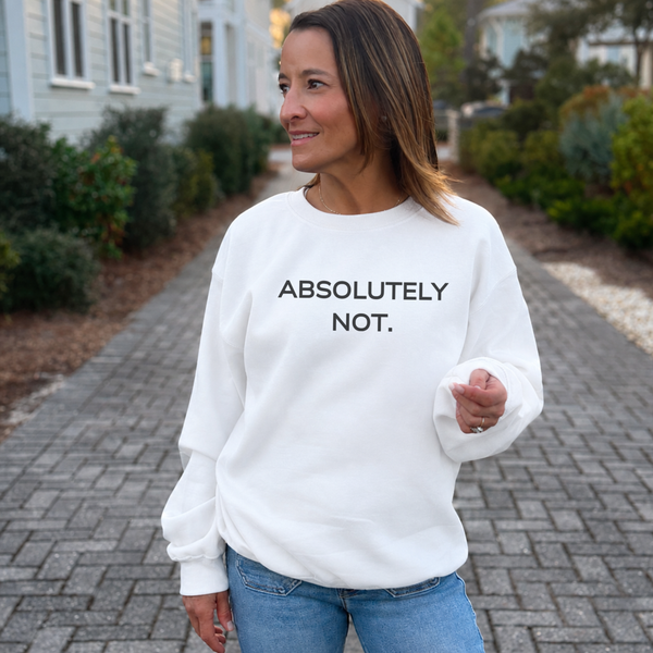 A woman wearing a white crewneck sweatshirt with the text 'ABSOLUTELY NOT.' printed in black across the chest, standing on a paved pathway outdoors.