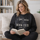Woman wearing a 'Anti-Social Book Club Members Only' sweatshirt, sitting on a couch with a book.