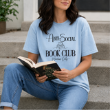 Person wearing a light blue t-shirt with 'Anti-Social Book Club Members Only' text, holding an open book.