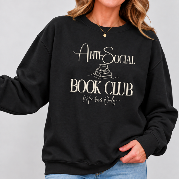 A woman wearing a black crewneck sweatshirt with a cream-colored graphic that reads 'Anti-Social Book Club Members Only' with a small illustration of stacked books. The photo is cropped from the chin down to the hips, showing the fit of the sweatshirt against a light gray background.
