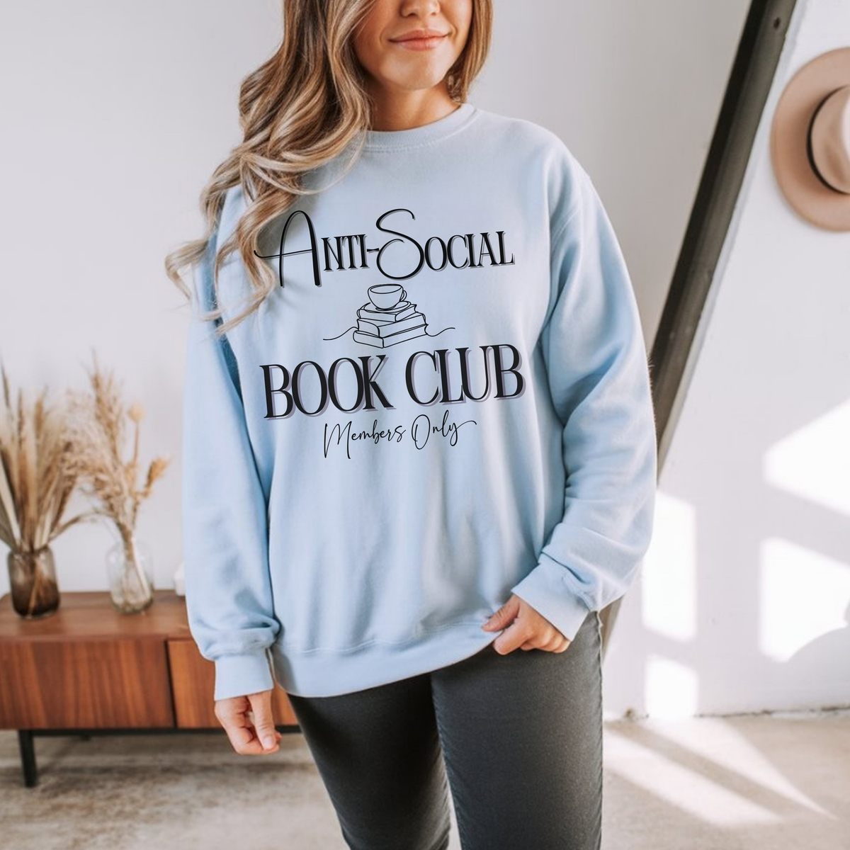 Person wearing a light blue sweatshirt with 'Anti-Social Book Club Members Only' text in a home setting.