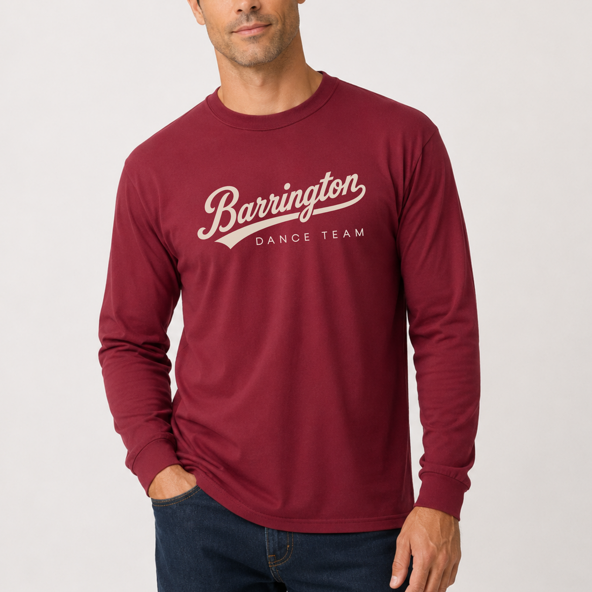 A man wearing a burgundy long-sleeve t-shirt with 'Barrington DANCE TEAM' printed in white script across the chest, paired with dark blue jeans, against a light gray studio background.