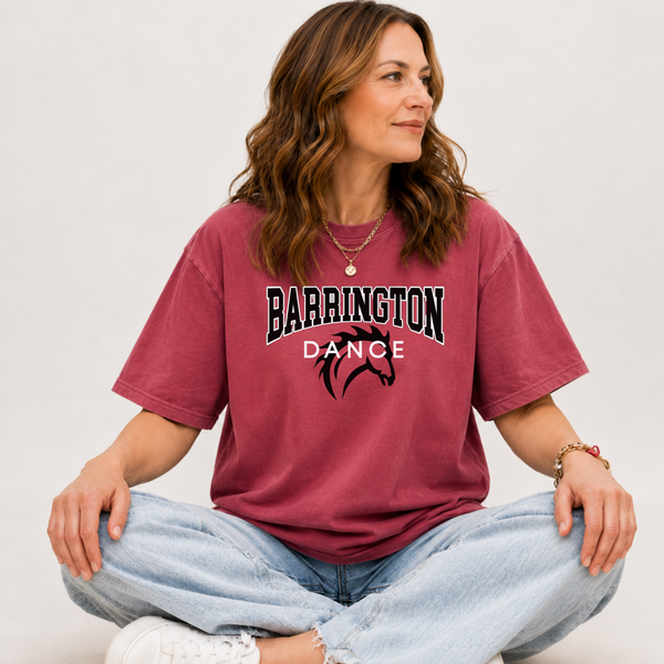 A woman sitting cross-legged wearing a faded burgundy t-shirt with 'BARRINGTON BRONCITIES' printed in black and white with a red silhouette, paired with light blue jeans and white sneakers.