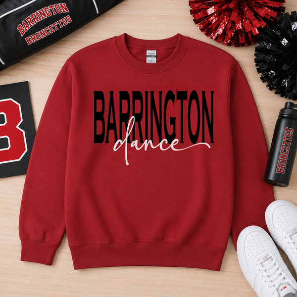 A red crewneck sweatshirt with 'BARRINGTON dance' printed on the front in black and white, laid flat on a light wood background with cheerleader pom-poms, a water bottle, and white sneakers.