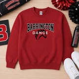 A red crewneck sweatshirt with 'BARRINGTON DANCE' and a horse graphic printed on the front, laid flat on a light wood surface with cheerleader pom-poms, a water bottle, and white sneakers around it.