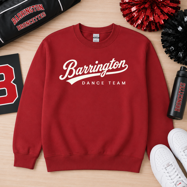 A red crewneck sweatshirt with 'Barrington DANCE TEAM' printed in white across the chest, styled in a flat lay on a light wood background with cheer pom-poms, a water bottle, sneakers, and a bag.