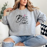 Woman wearing a gray sweatshirt with 'Bless your Heart' text sitting on a couch.