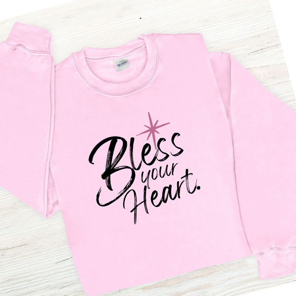 Pink sweatshirt with 'Bless your Heart' text on a light wooden surface