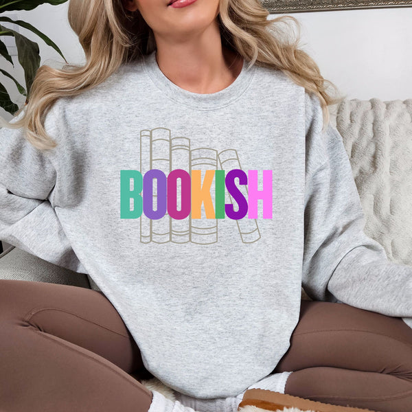 Woman wearing a gray sweatshirt with 'BOOKISH' in colorful letters, sitting on a couch.