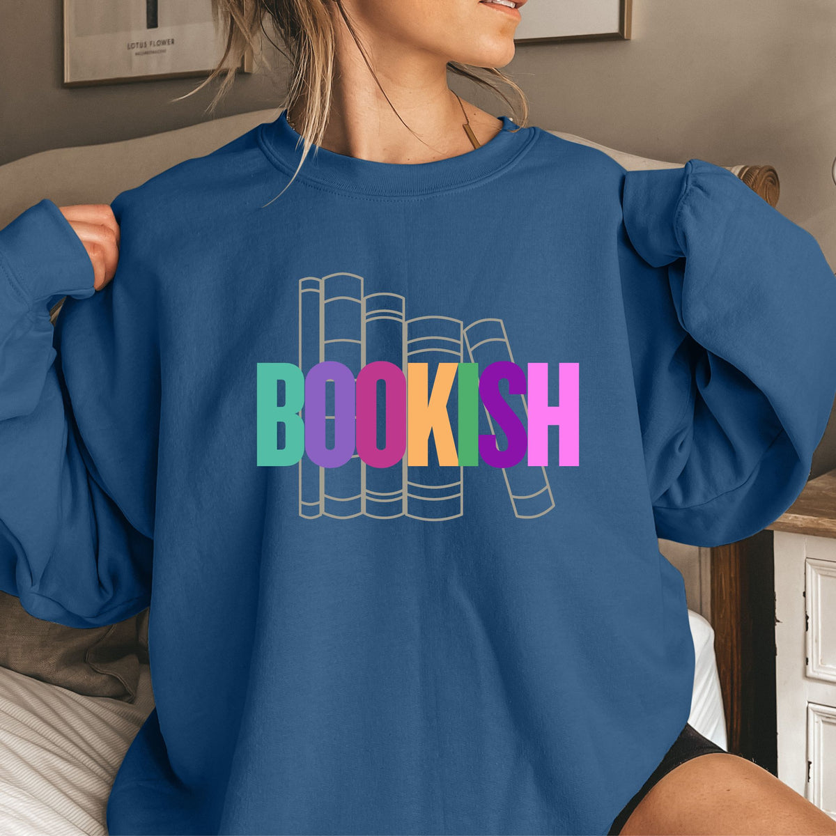 Person wearing an indigo blue sweatshirt with 'BOOKISH' text in colorful letters.