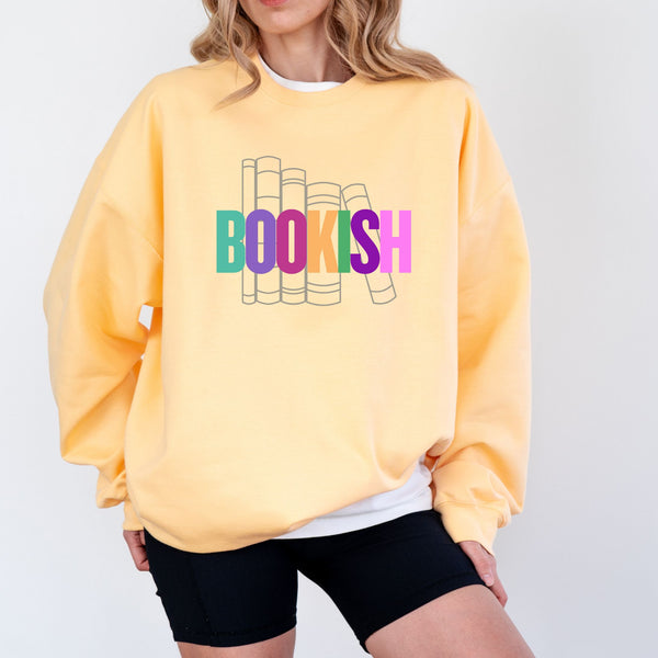 Person wearing a yellow sweatshirt with 'BOOKISH' colorful text and book illustrations on a plain background