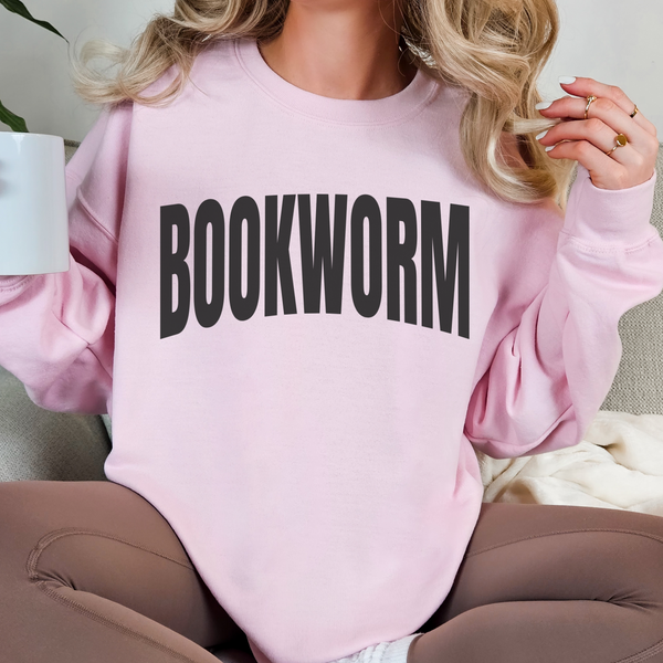 Person wearing a pink sweatshirt with 'BOOKWORM' text, holding a book.