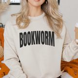 Person wearing a beige sweatshirt with 'BOOKWORM' text, holding a coffee cup.