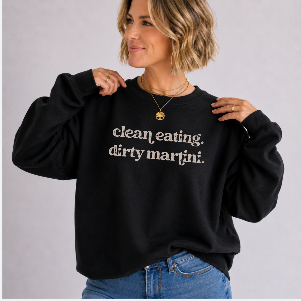 A woman wearing a black crewneck sweatshirt with the text 'clean eating. dirty martini.