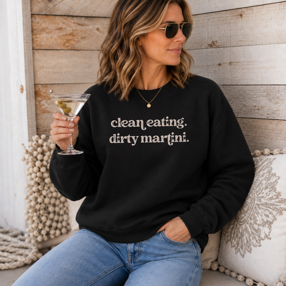A woman wearing a black crewneck sweatshirt with the text 'clean eating. dirty martini.