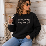 A woman wearing a black crewneck sweatshirt with the text 'clean eating. dirty martini.