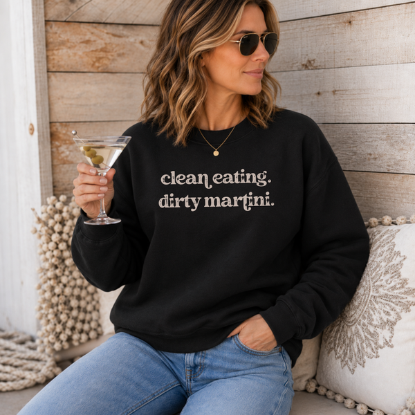 A woman wearing a black crewneck sweatshirt with the text 'clean eating. dirty martini.