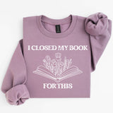 Purple sweatshirt with 'I Closed My Book For This' text and floral design on a white background