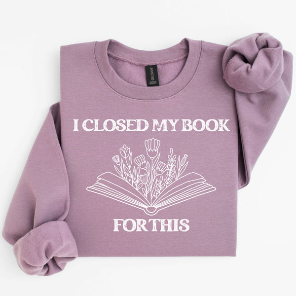 Purple sweatshirt with 'I Closed My Book For This' text and floral design on a white background