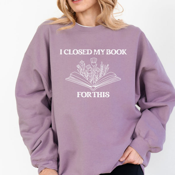Person wearing a purple sweatshirt with a book-themed design and text that reads "I CLOSED MY BOOK FOR THIS."