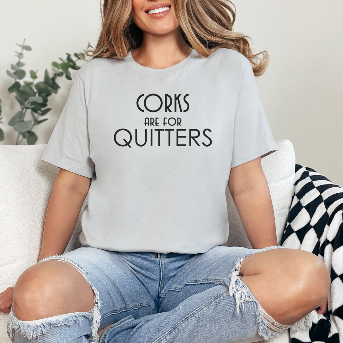 Person wearing a light gray t-shirt with 'Corks are for Quitters' text, sitting on a couch.