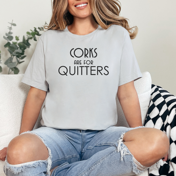 Person wearing a light gray t-shirt with 'Corks are for Quitters' text, sitting on a couch.
