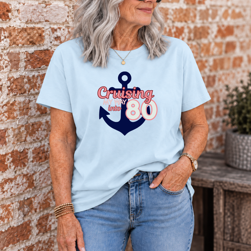 A woman wearing a light blue graphic t-shirt with a navy blue anchor and the words 'Cruising in style 80' in red and pink, standing in front of a brick wall.