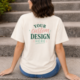 Person wearing a white t-shirt with 'Your custom design here' text, sitting on steps.