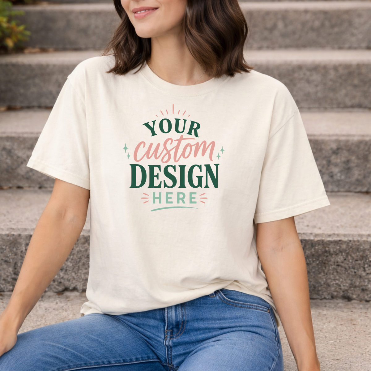 Person wearing a white t-shirt with 'Your custom design here' text, sitting on steps.