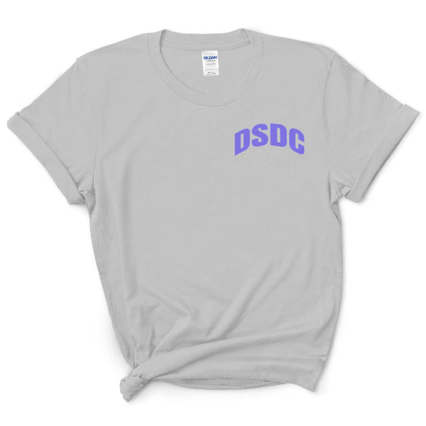 A light gray short-sleeve t-shirt with 'DSDC' printed in purple arched lettering on the left chest, styled with a knot at the bottom hem on a white background.