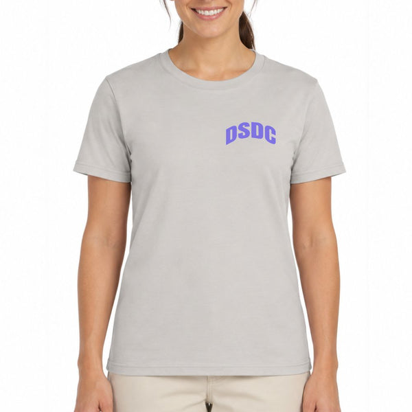 A woman wearing a light gray crewneck t-shirt with the letters 'DSDC' printed in purple on the left chest, paired with light beige pants, against a plain white background.
